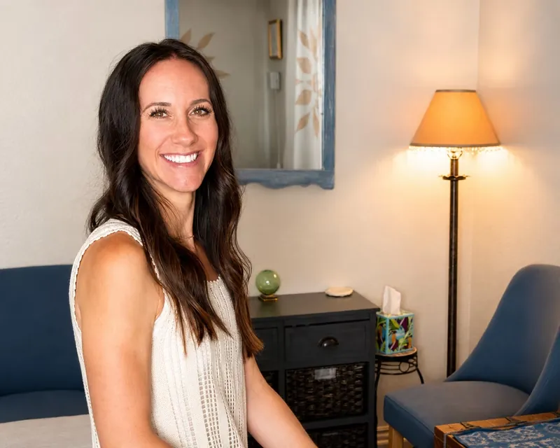 Amy Balaam in the Rooted Wellness Method studio at 534 Oak St, with a soft lamp, armchair and massage table